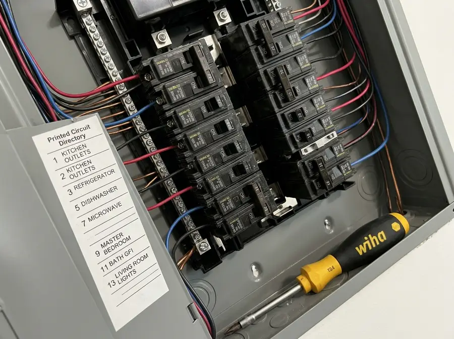 Tight diagonal crop of a finished 200-amp panel interior with two rows of labeled breakers, a printed circuit directory and a torque screwdriver resting on the panel lip, everything installed and connected